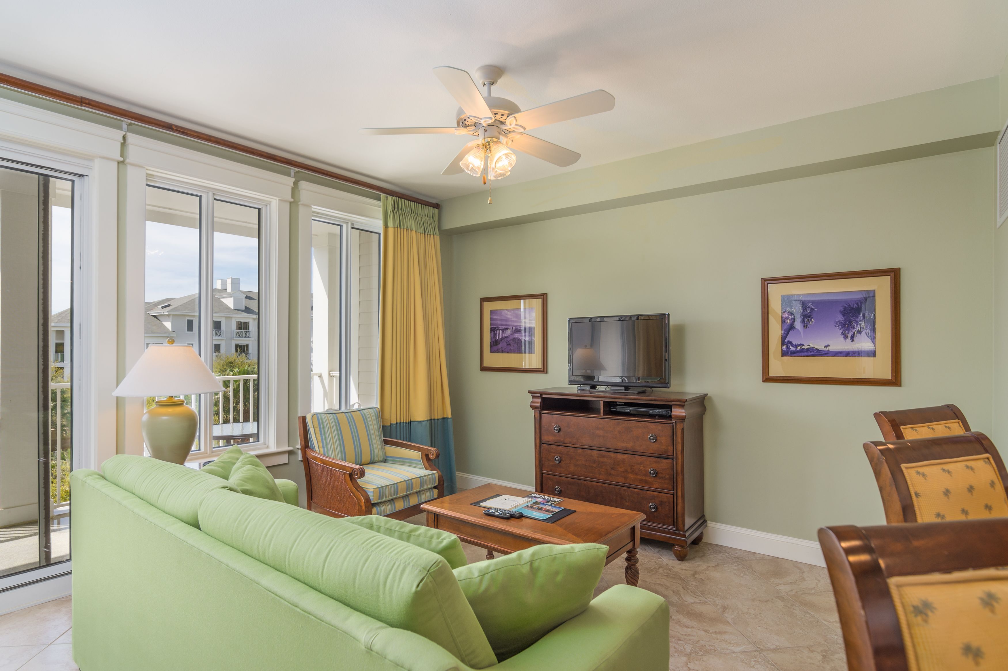A living room with a green sofa, a wooden coffee table, a television on a wooden cabinet, and two framed pictures on the wall.