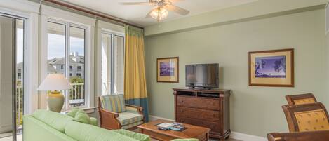 A living room with a green sofa, a wooden coffee table, a television on a wooden cabinet, and two framed pictures on the wall.