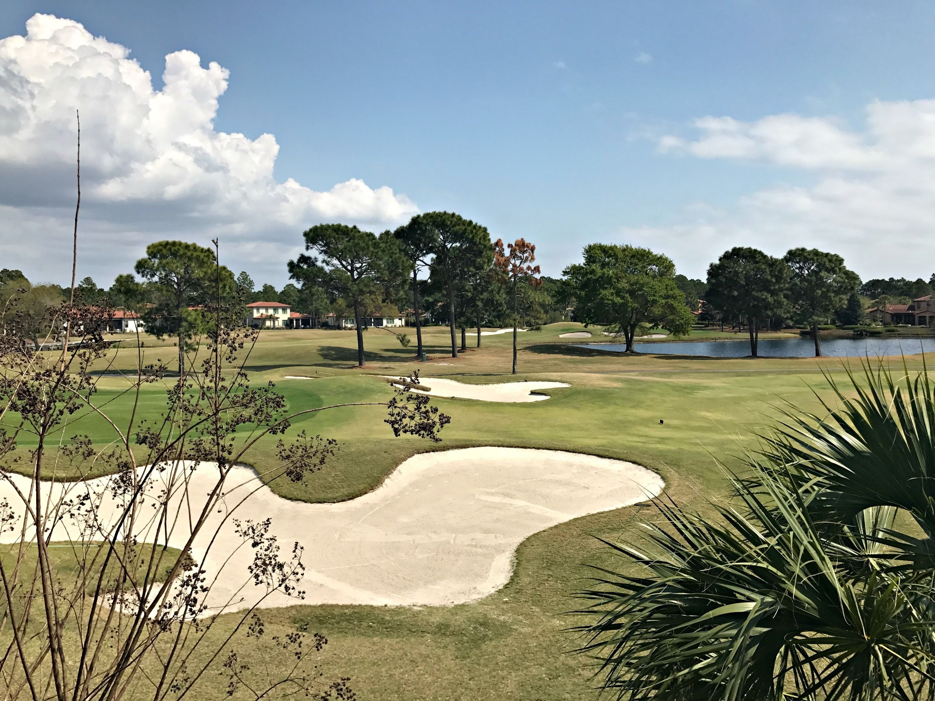 Un parcours de golf avec des bunkers de sable, des arbres et un plan d’eau.