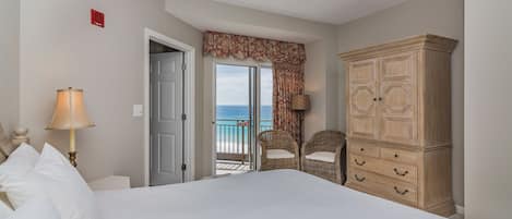 Une chambre avec un grand lit, une armoire, deux fauteuils en osier, une lampe et une vue sur la mer par une porte.