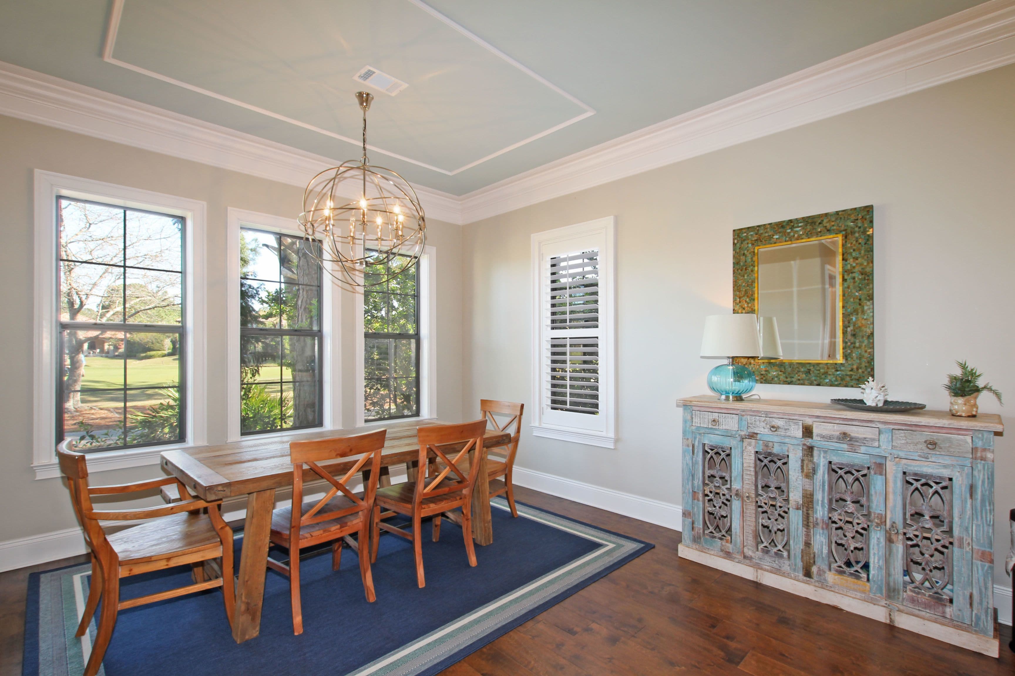 A dining area with a wooden table and chairs, a blue rug, and a decorative cabinet with a mirror.