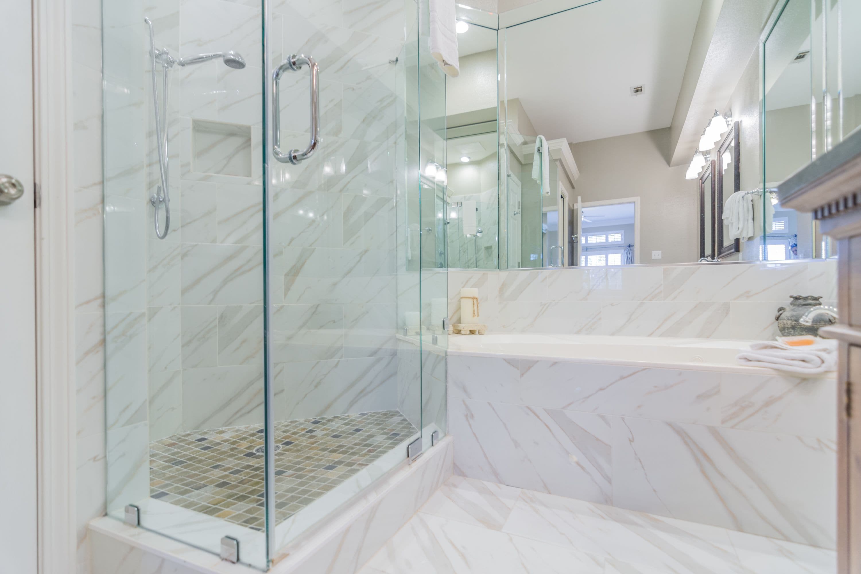 A modern bathroom with a glass-enclosed shower, a marble-tiled tub, and a large mirror.