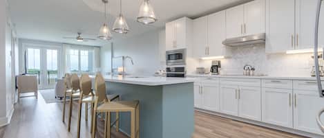 Una cocina moderna con gabinetes blancos, una isla central e iluminación colgante.