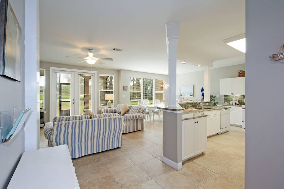 A spacious living area with a striped sofa, a dining table, and a kitchen with white cabinets and a central island.