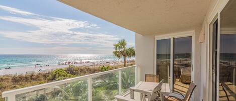 A balcony with a view of the beach, outdoor furniture, and a glass door leading to the interior.