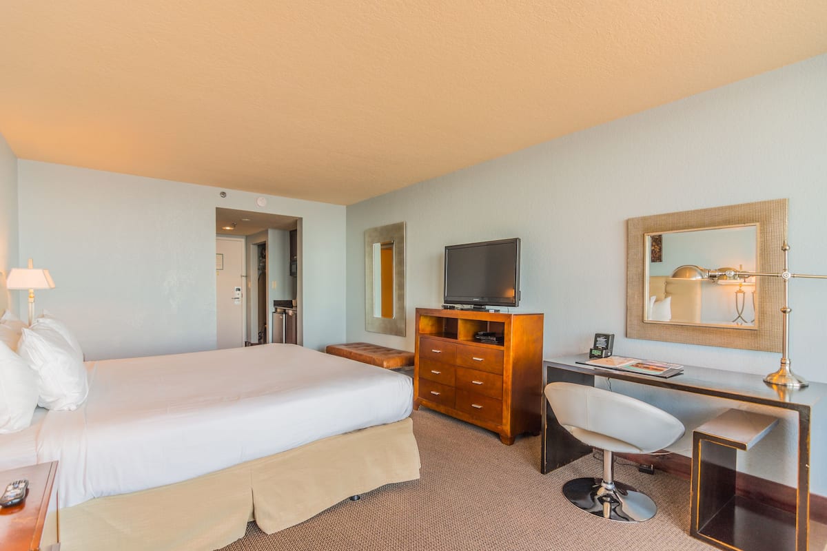 A hotel room with a bed, a desk, a chair, a dresser, a television, and a mirror.