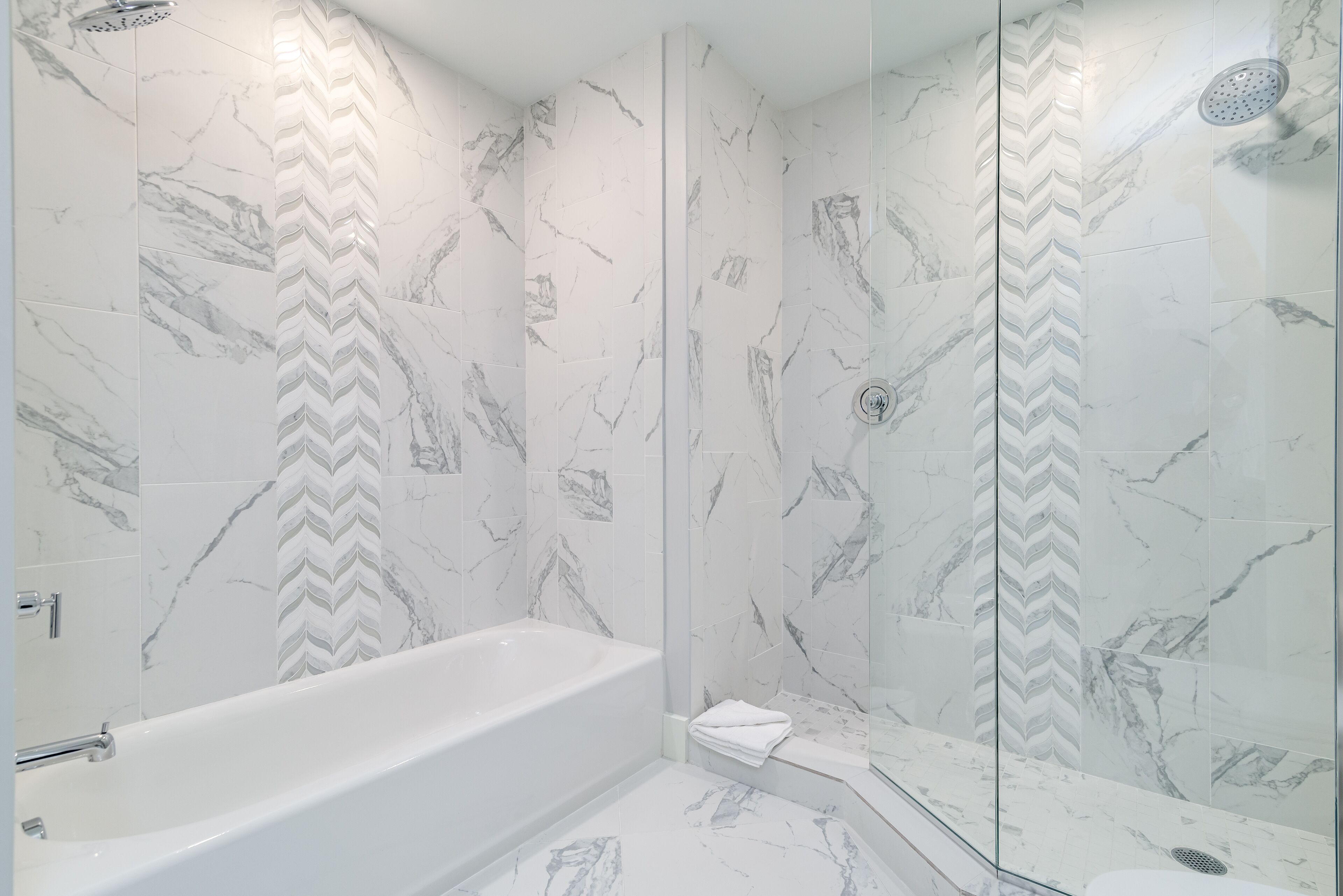 A modern bathroom with a freestanding bathtub, a glass-enclosed shower, and marble-patterned walls.
