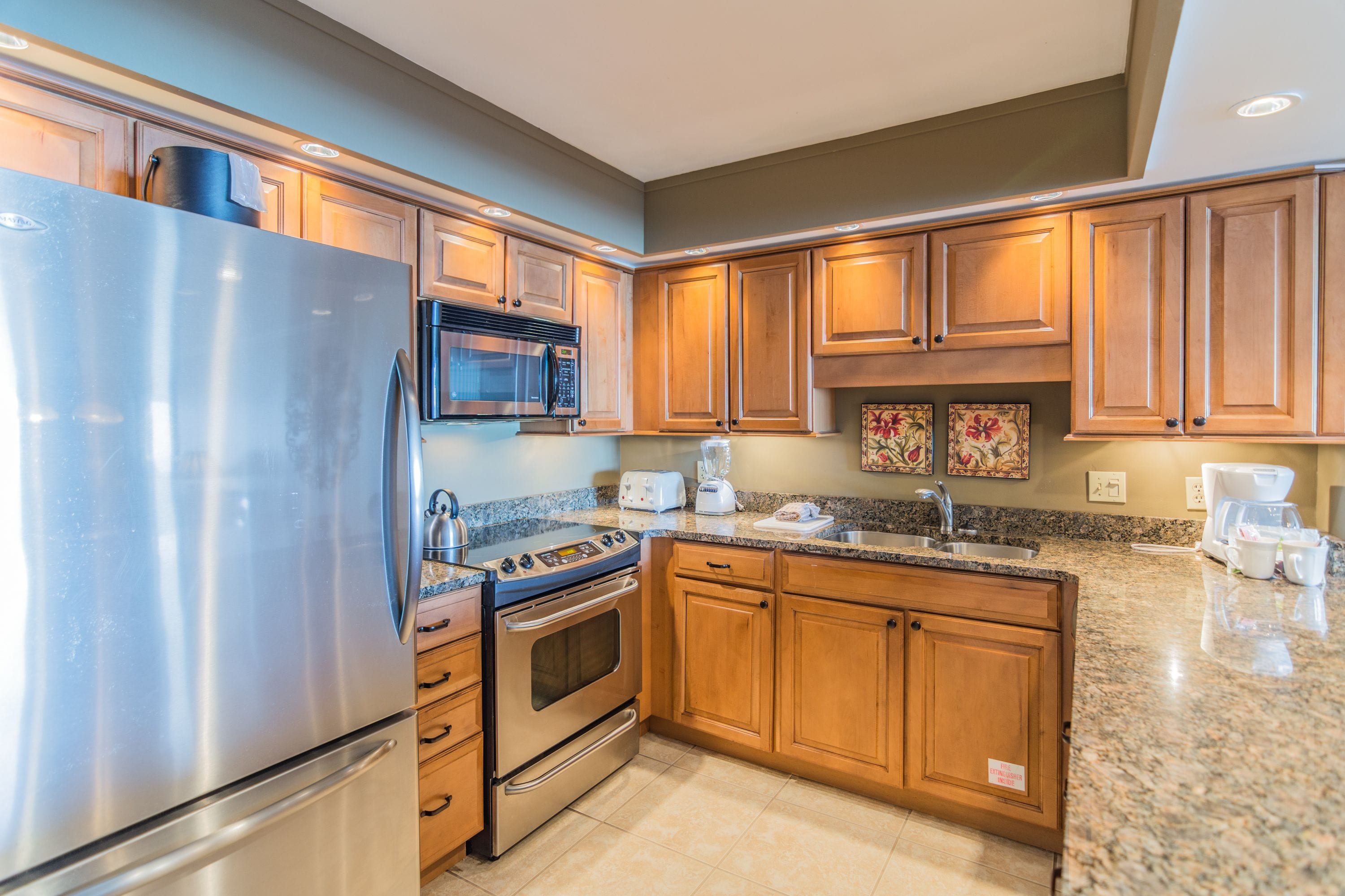 A modern kitchen with stainless steel appliances, wooden cabinets, granite countertops, and a built-in microwave.