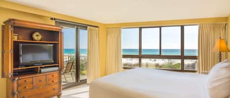Un dormitorio con una cama grande, un aparador de madera, un televisor y vista a la playa.