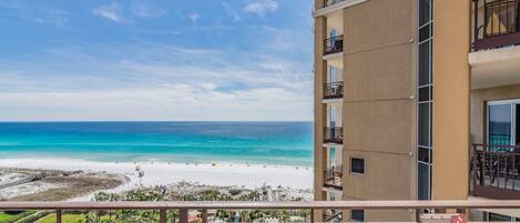 A high-rise hotel with balconies overlooking a beach and a pool area.