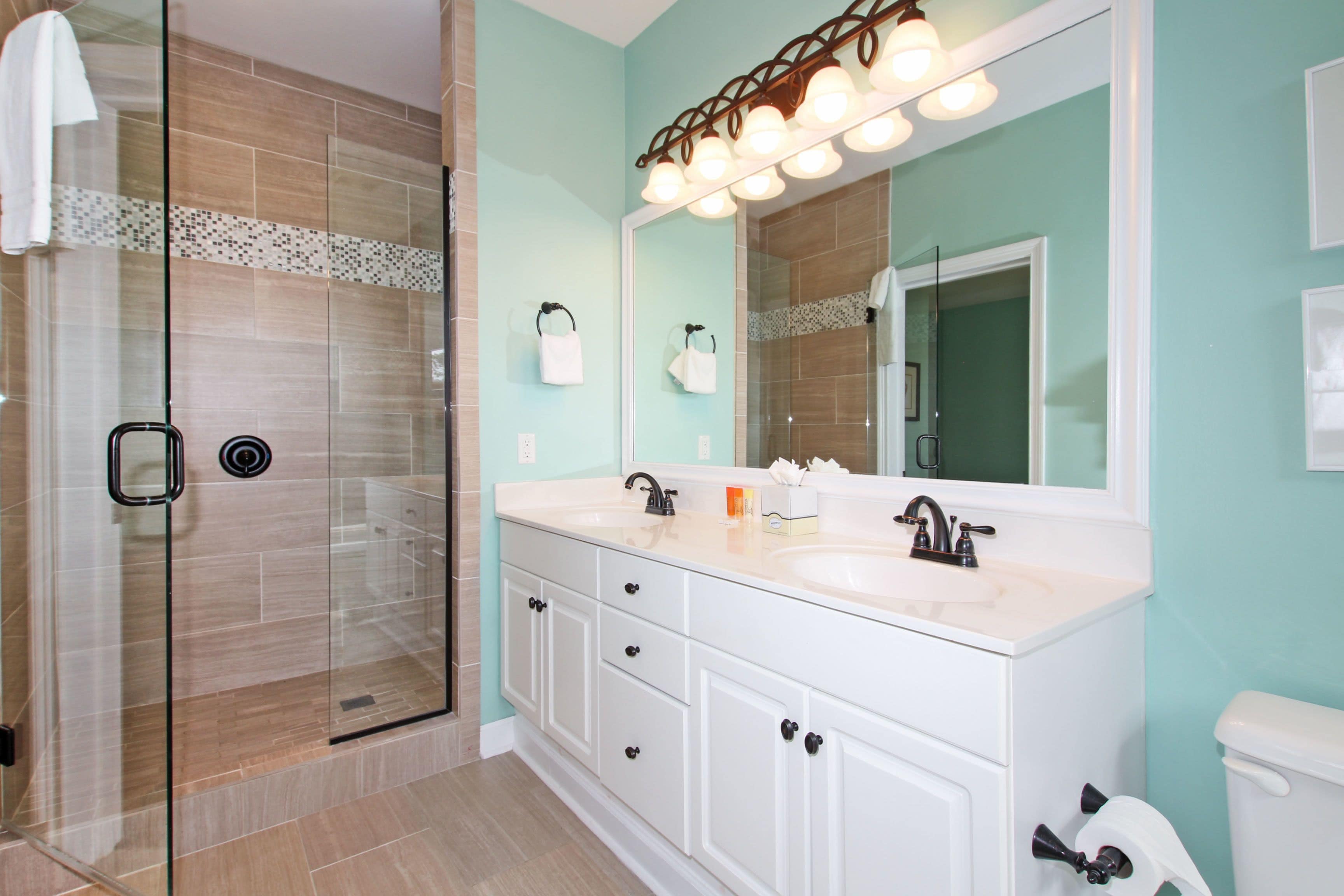 A modern bathroom with a glass shower enclosure, a white vanity with a large mirror, and a toilet.