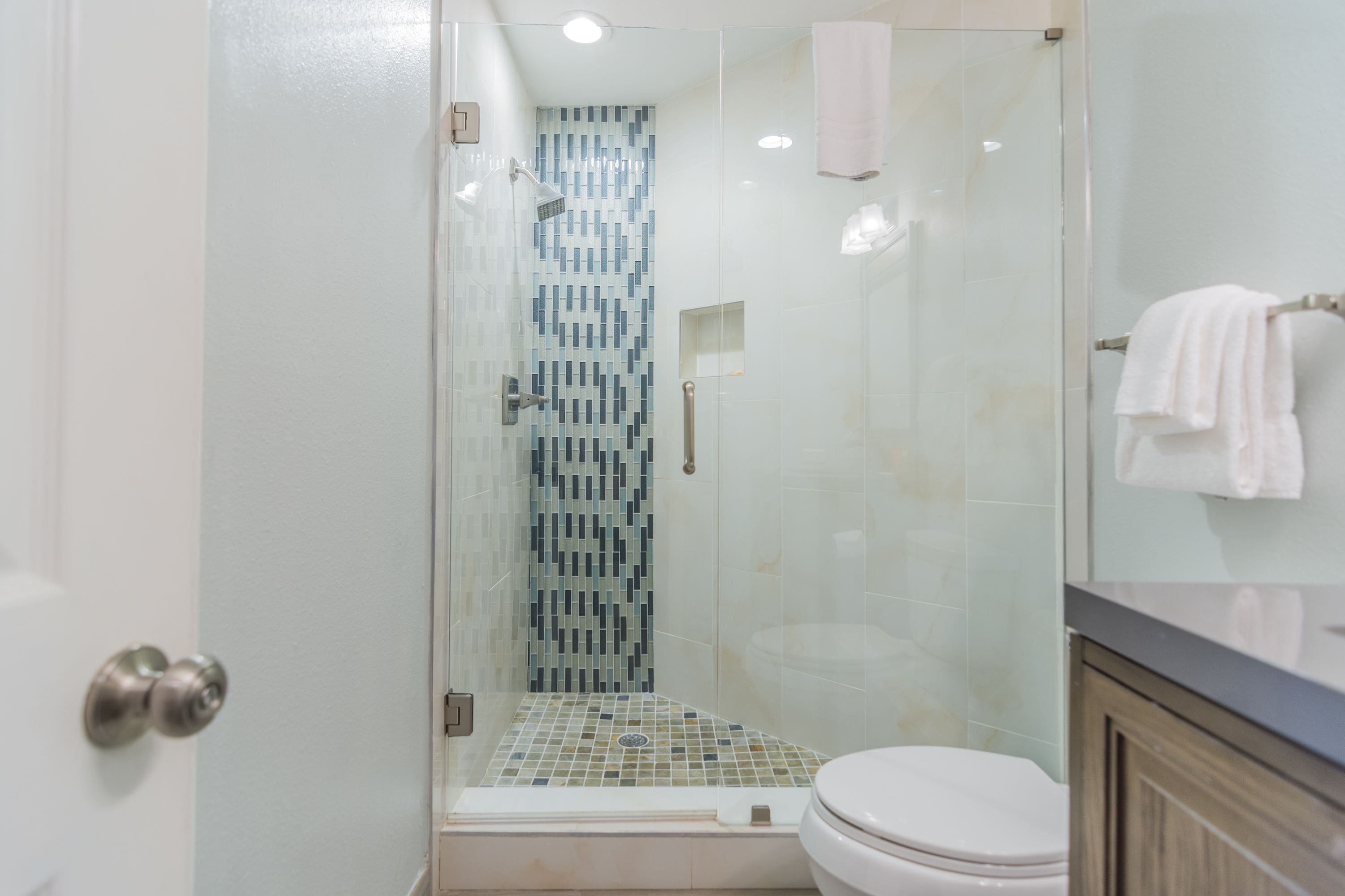 A modern bathroom with a glass-enclosed shower, a toilet, and a vanity with a towel rack.