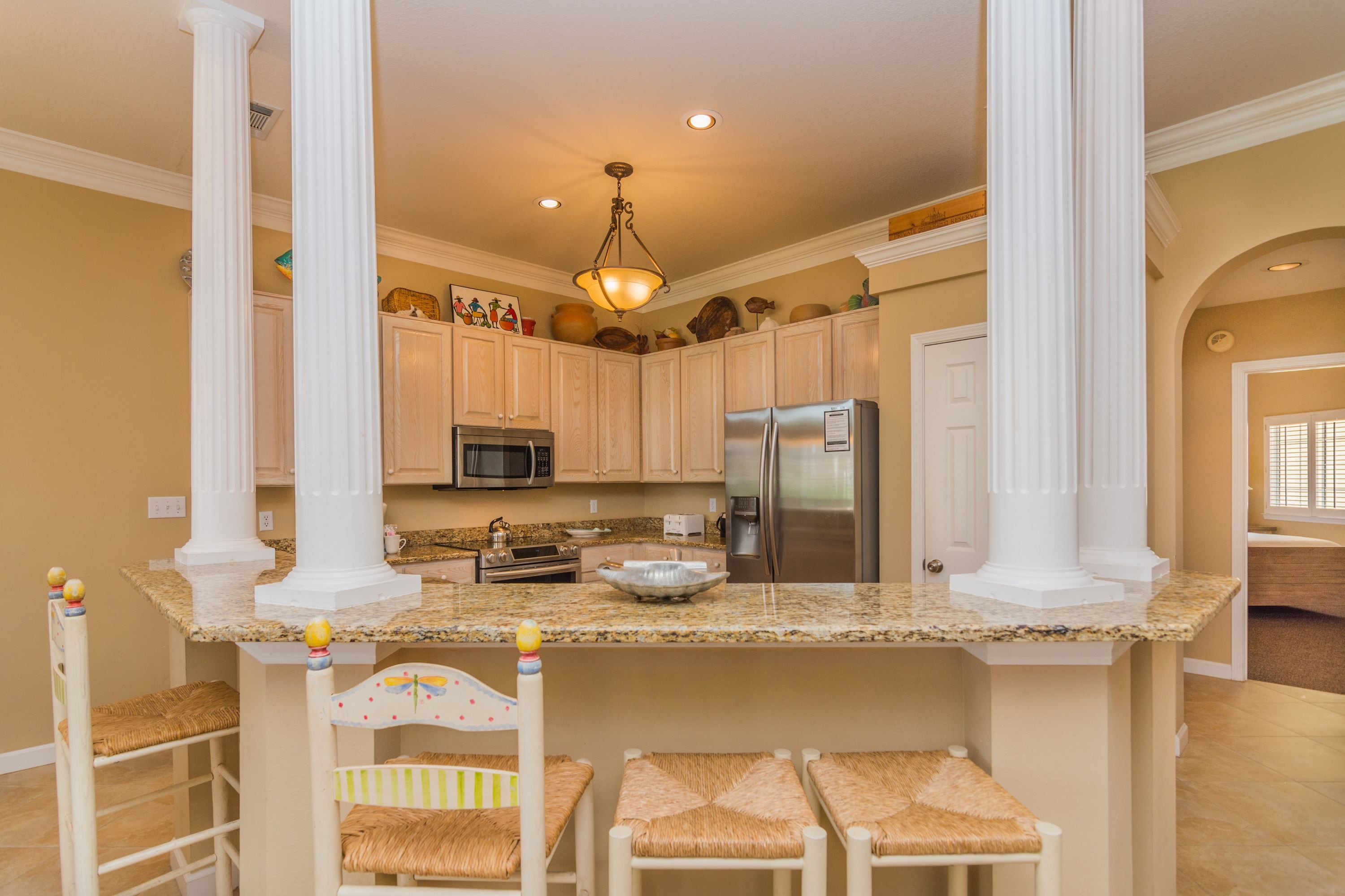 A kitchen with white cabinetry, granite countertops, a stainless steel refrigerator, and a hanging light fixture.