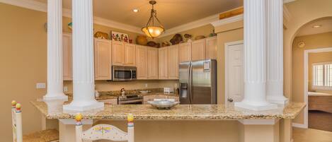 A kitchen with white cabinetry, granite countertops, a stainless steel refrigerator, and a hanging light fixture.