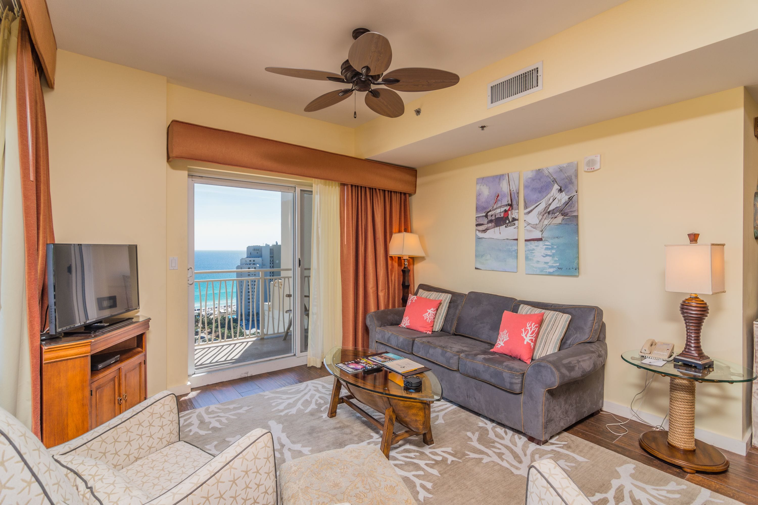 A living room with a sofa, television, and a balcony with a view of the ocean.