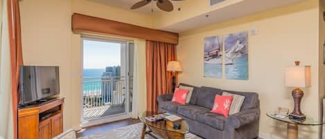 Un salon avec un canapé, une télévision et un balcon offrant une vue sur l’océan.