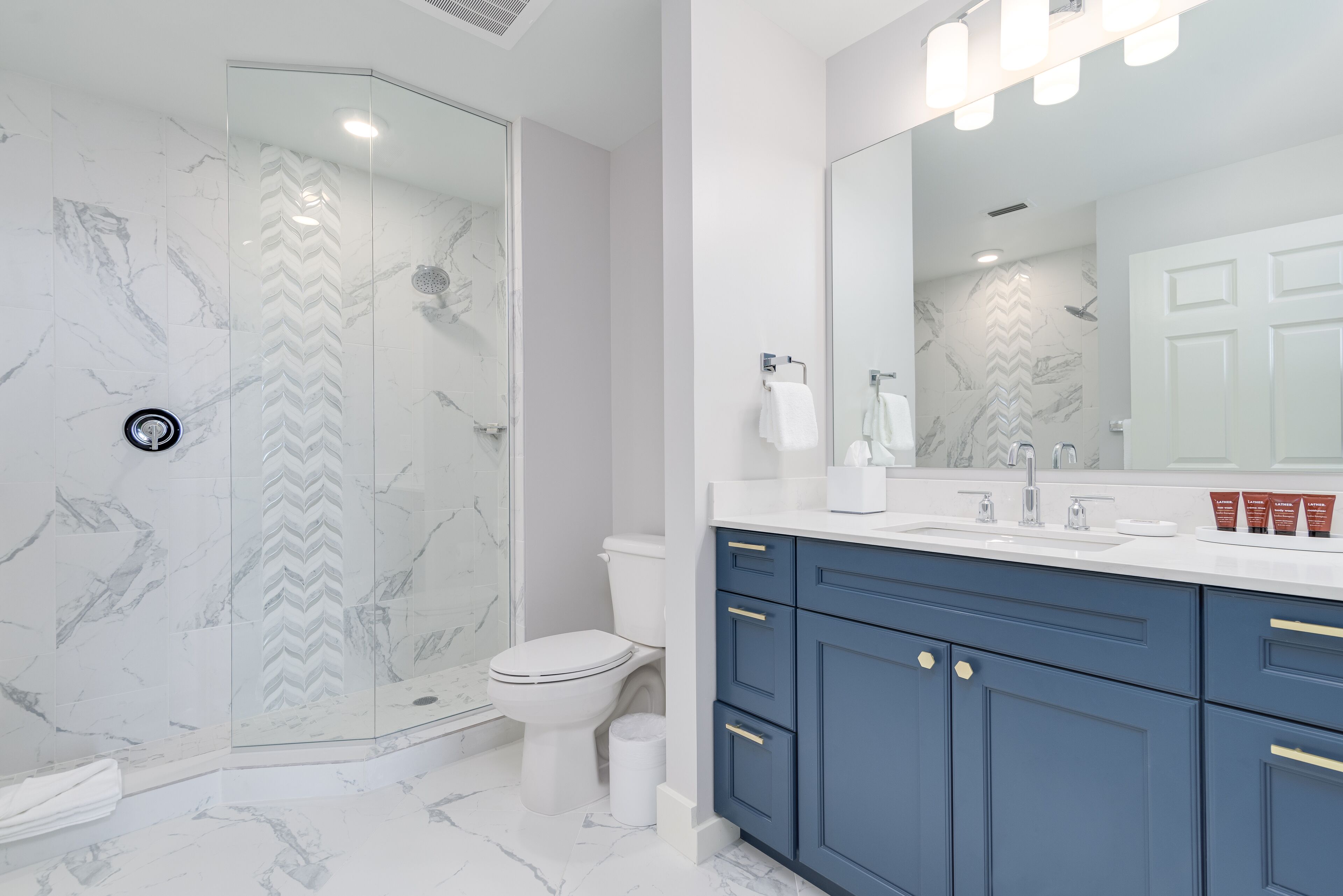 A modern bathroom with a glass-enclosed shower, a white toilet, and a vanity with blue cabinets and gold handles.