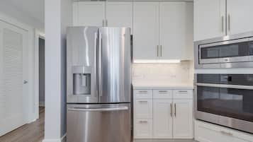 A modern kitchen with stainless steel appliances, white cabinetry, and a herringbone tile backsplash.