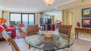 A spacious living room with a glass dining table, comfortable seating, a television, and a view of the ocean. - Sandestin Golf and Beach Resort (Miramar Beach)
