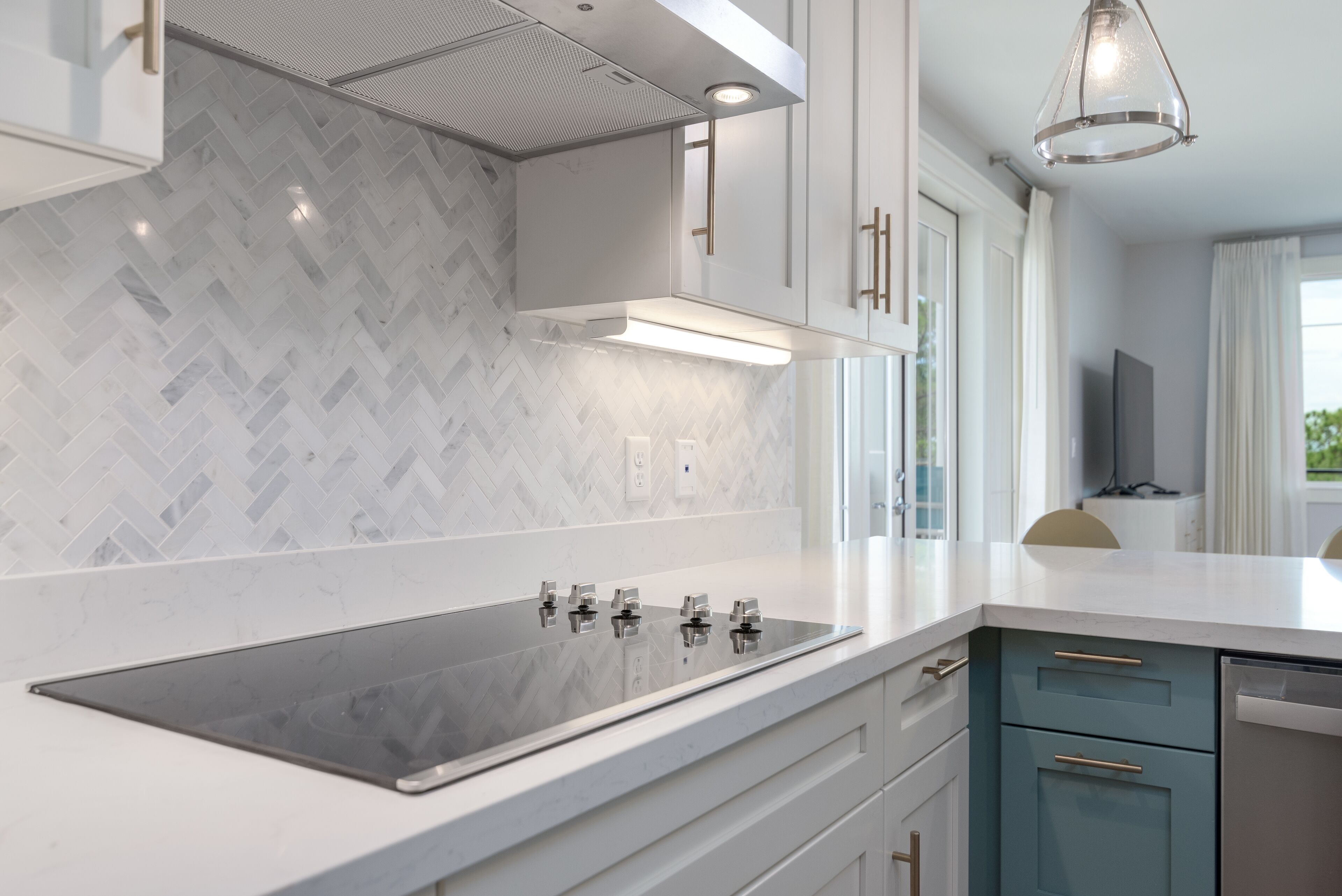A modern kitchen with a herringbone tile backsplash, stainless steel appliances, and white cabinetry.