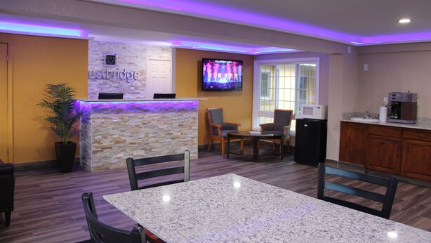 A reception area with a stone counter, a television mounted on the wall, and a seating area with chairs and a table. - Westbridge Inn and Suites (Clinton)