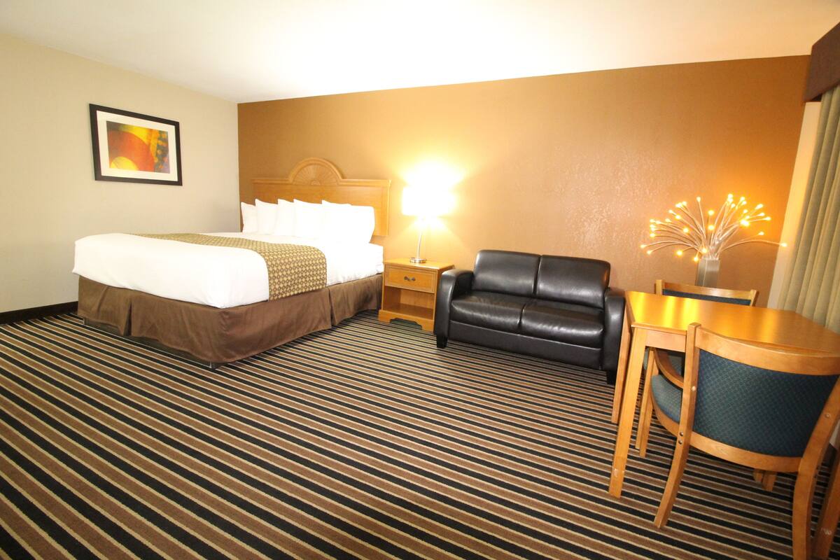 A hotel room with a bed, a desk, a chair, a lamp, and a decorative wall piece.