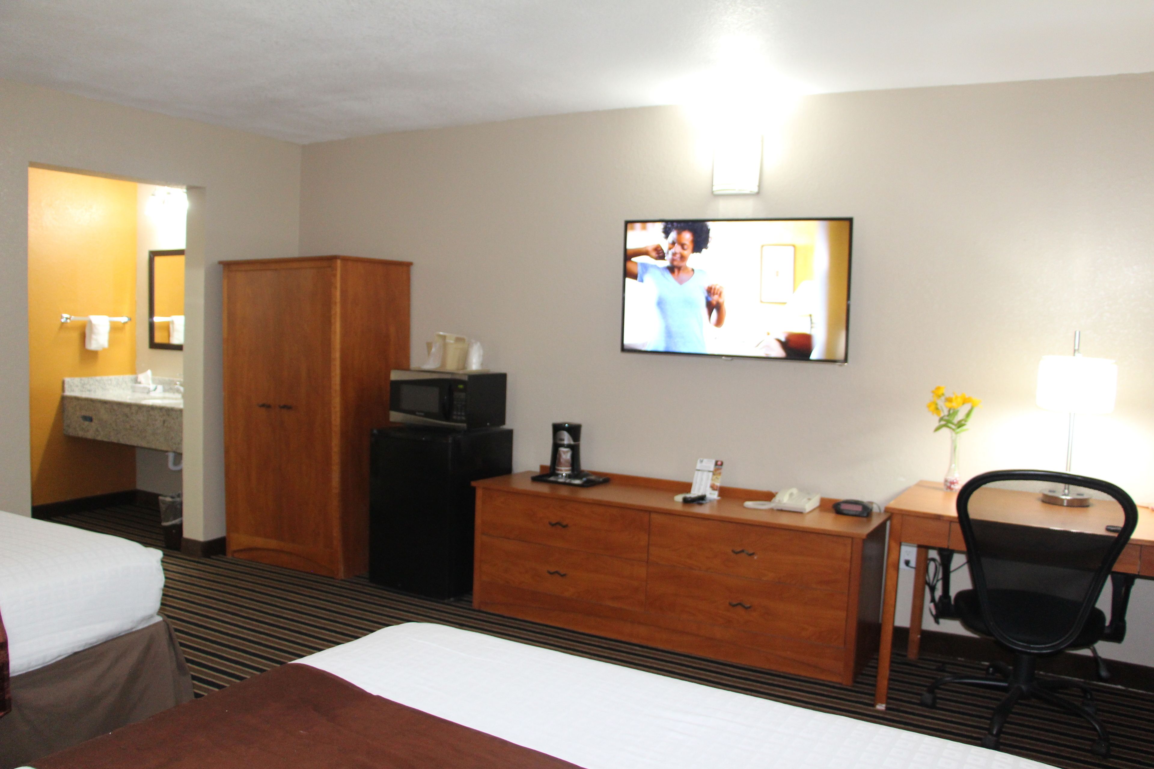 A hotel room with a bed, a desk, a chair, a television, and a wooden wardrobe.
