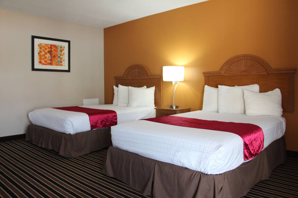 A hotel room with two beds, a nightstand with a lamp, and a framed picture on the wall.
