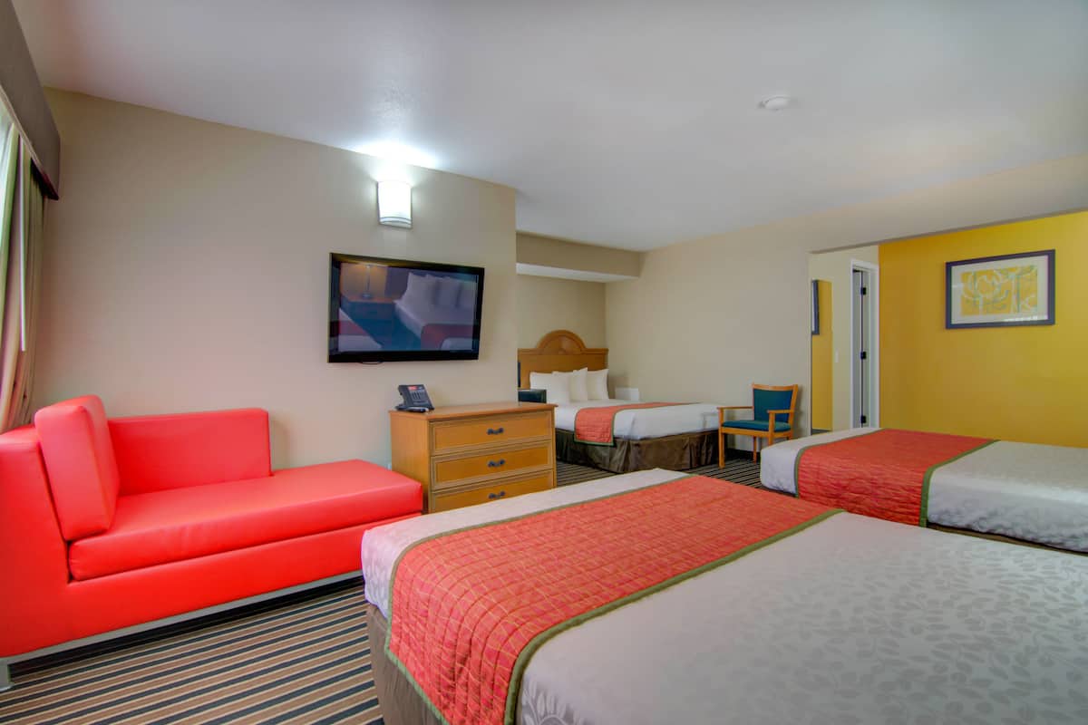 A hotel room with a red sofa, two beds with red and white bedding, a wooden dresser, a television, and a framed picture on the wall.
