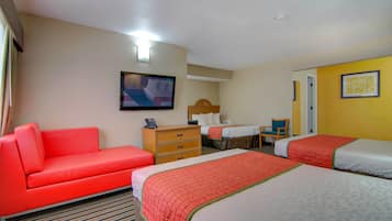 Habitación de hotel con un sofá rojo, dos camas con ropa de cama roja y blanca, un aparador de madera, un televisor y un cuadro en la pared.