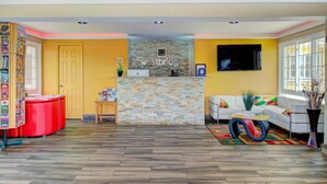 A reception area with a stone wall, a white sofa, a red table, and a bookshelf filled with magazines. - Westbridge Inn and Suites (Clinton)
