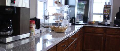 Una cocina con cafetera, refrigerador, microondas y frutero.
