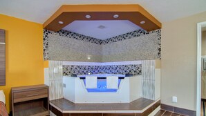 A modern bathroom with a built-in bathtub, a wooden nightstand, and a tiled floor. - Westbridge Inn and Suites (Clinton)