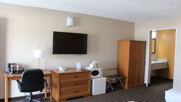 A hotel room with a bed, a desk with a chair, a television, a microwave, a refrigerator, a wardrobe, and a bathroom with a sink and mirror.