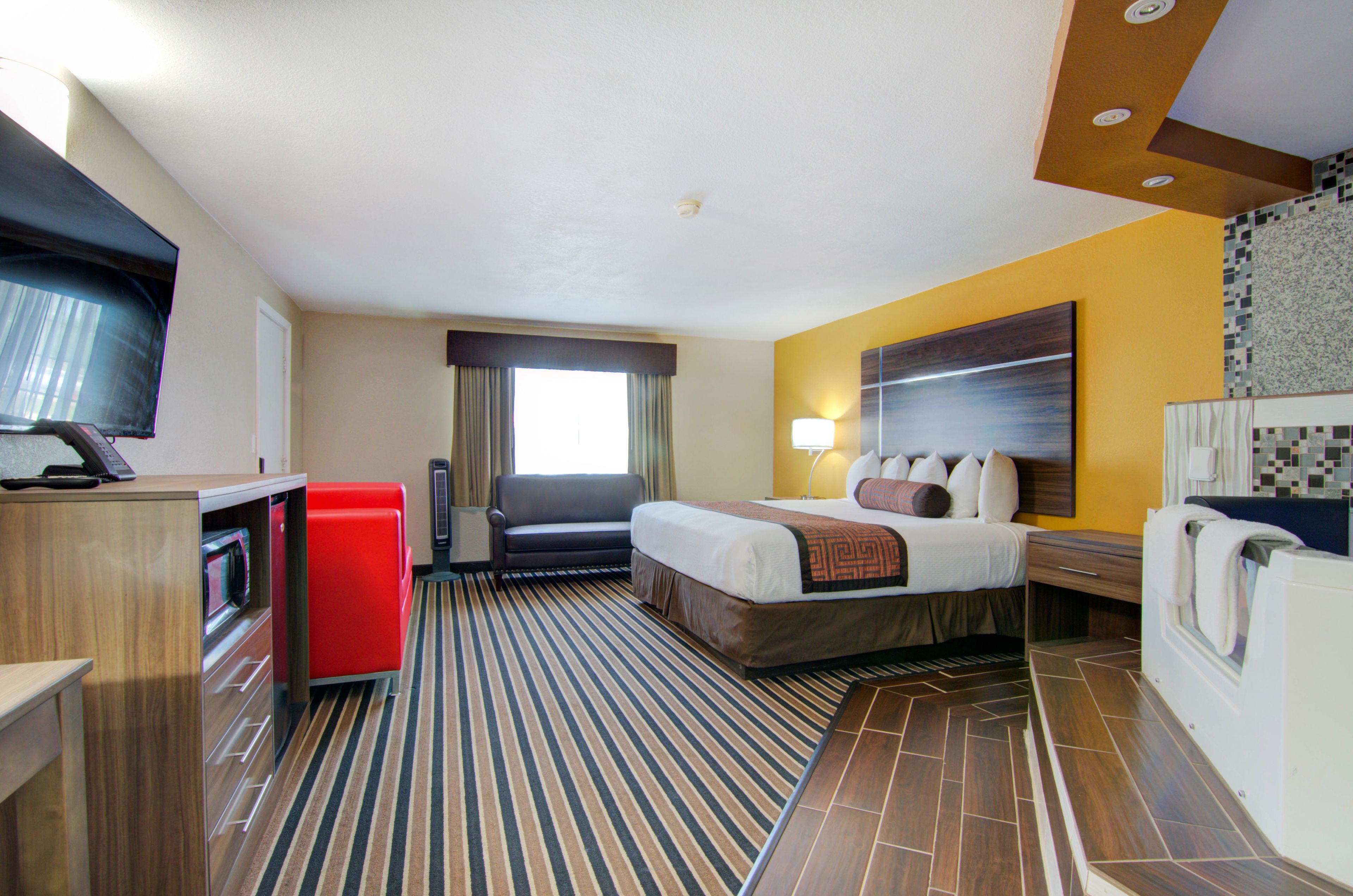 A hotel room with a bed, a desk with a computer, a red refrigerator, a television, and a bathroom with a shower and toilet.