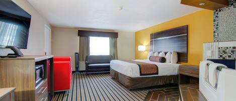 A hotel room with a bed, a desk with a computer, a red refrigerator, a television, and a bathroom with a shower and toilet.