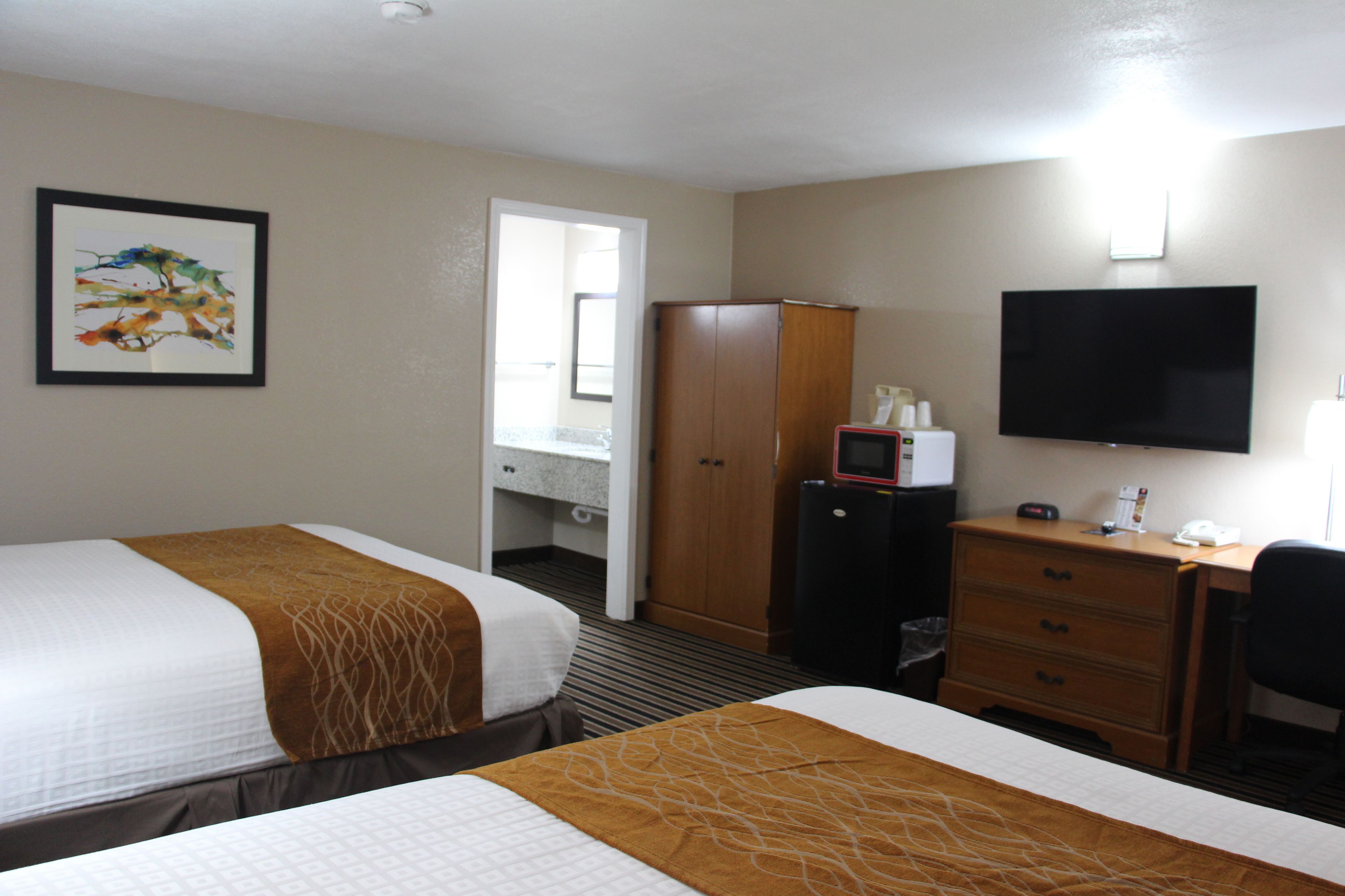 A hotel room with two beds, a desk, a television, a wardrobe, and a bathroom visible through an open door.
