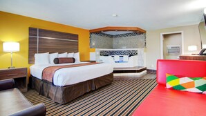 A hotel room with a bed, a desk, a chair, a red couch, a bathroom with a shower, and a mirror. - Westbridge Inn and Suites (Clinton)