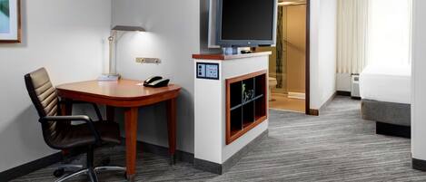 A hotel room with a flat-screen TV, a desk with a chair, a fireplace, a bed, and a staircase leading to another room.