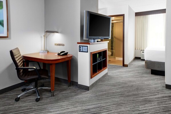 A hotel room with a flat-screen TV, a desk with a chair, a fireplace, a bed, and a staircase leading to another room.