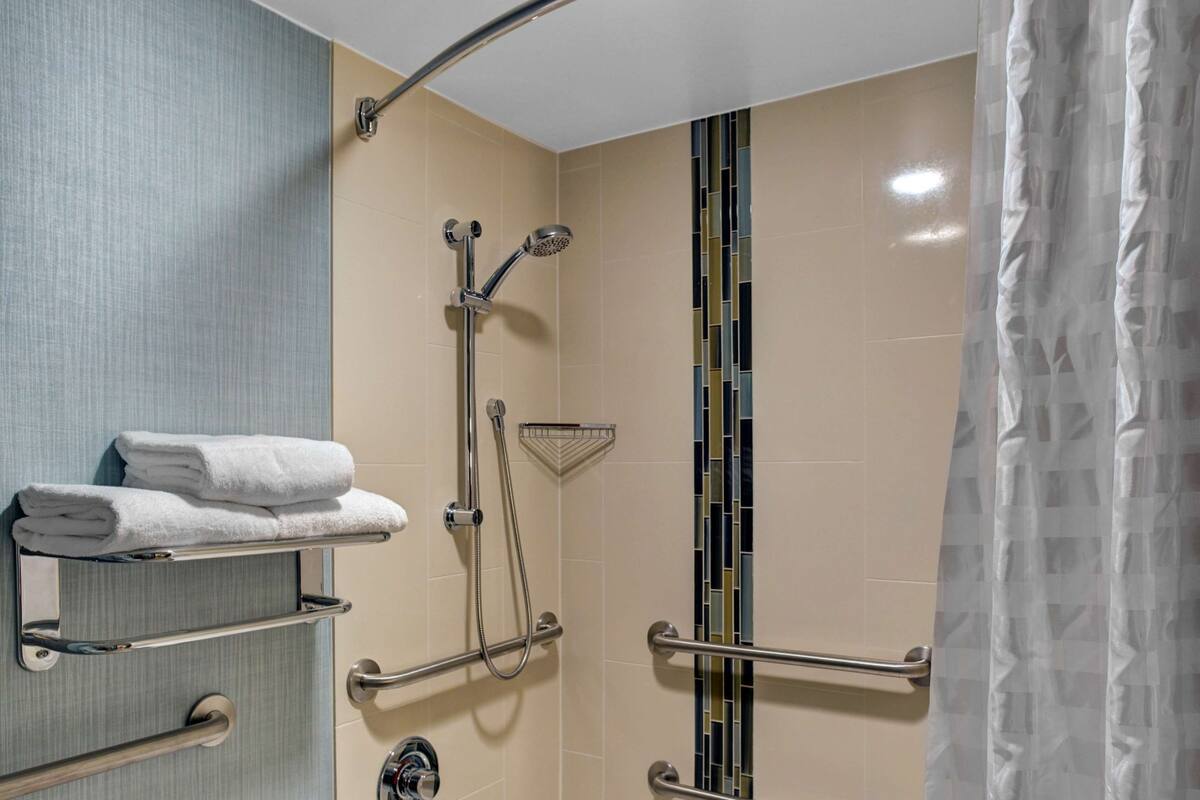A modern bathroom with a bathtub, grab bars, a showerhead, and a towel rack.