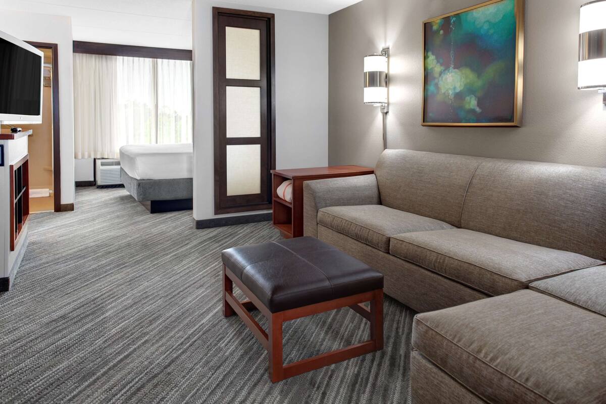 A hotel room with a sofa, a small wooden table, a TV, a bed, and a painting on the wall.