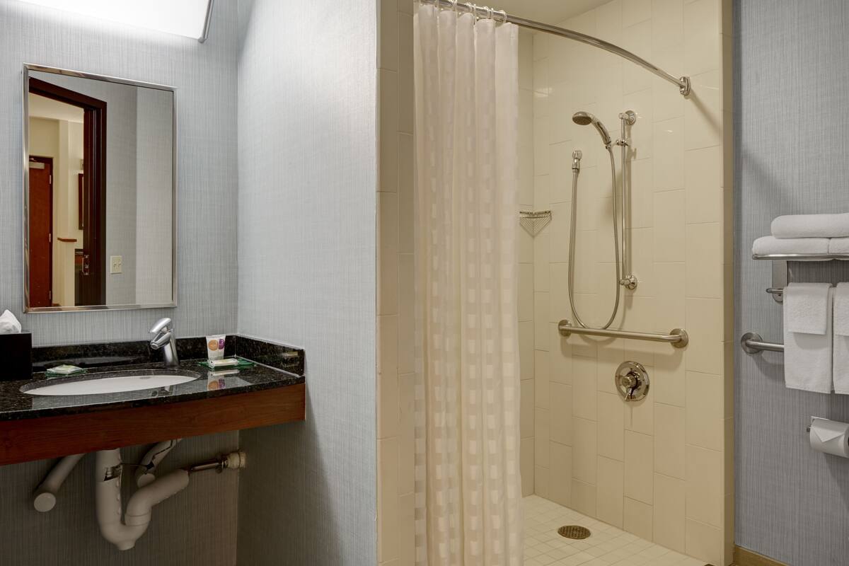 A bathroom with a sink, mirror, shower, and towel rack.