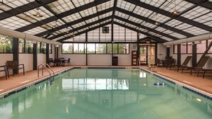 An indoor swimming pool with clear water, surrounded by lounge chairs and tables, under a high ceiling with a grid pattern. - Hyatt Place Denver Airport (Aurora)