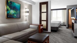 A hotel room with a sofa, a small table, a bed, a TV, and a painting on the wall. - Hyatt Place Denver Airport (Aurora)