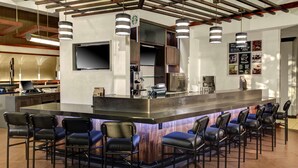 A modern bar area with a central island, bar stools, a flat-screen TV, and a menu board. - Hyatt Place Denver Airport (Aurora)