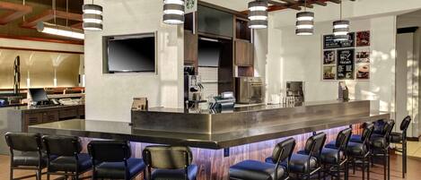 A modern bar area with a central island, bar stools, a flat-screen TV, and a menu board.