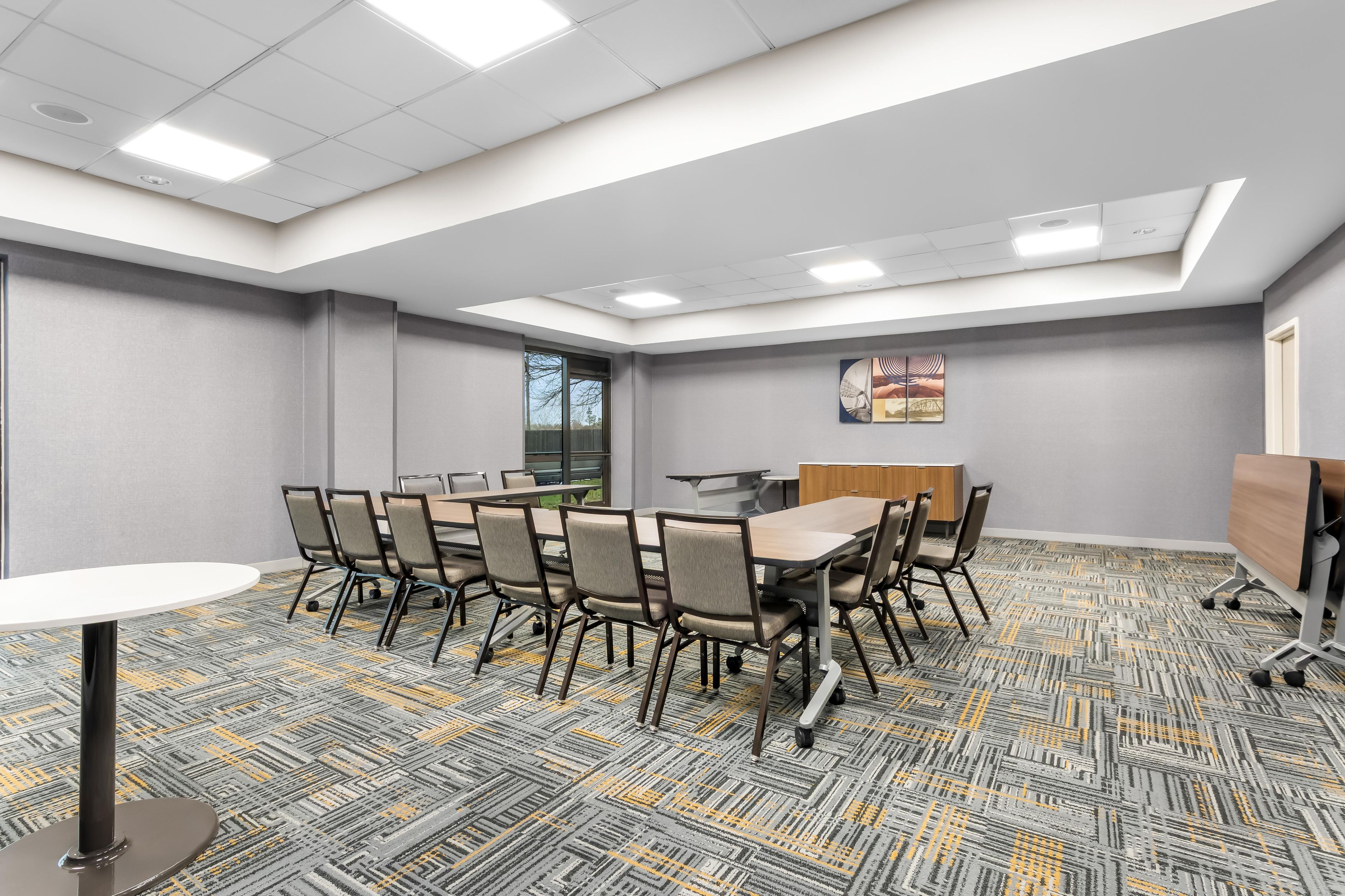 A conference room with a long table, chairs, a whiteboard, and a carpeted floor.