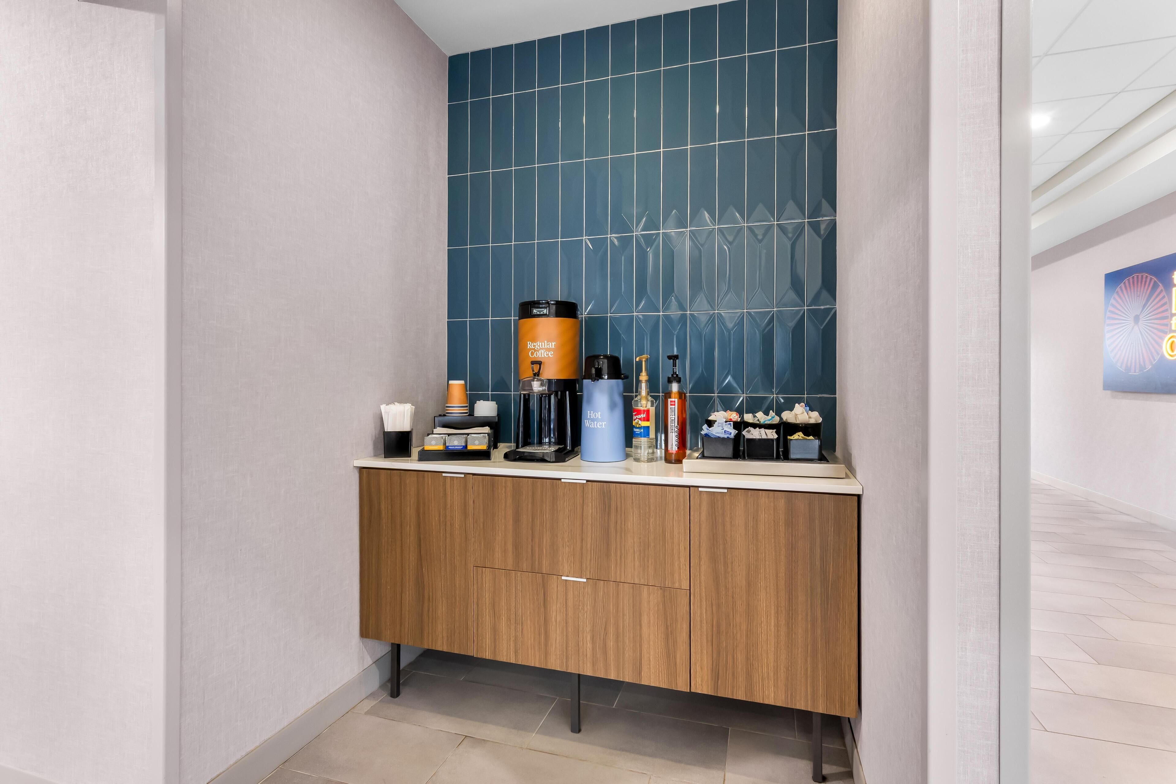 A modern bathroom with a wooden vanity, a coffee maker, and toiletries.