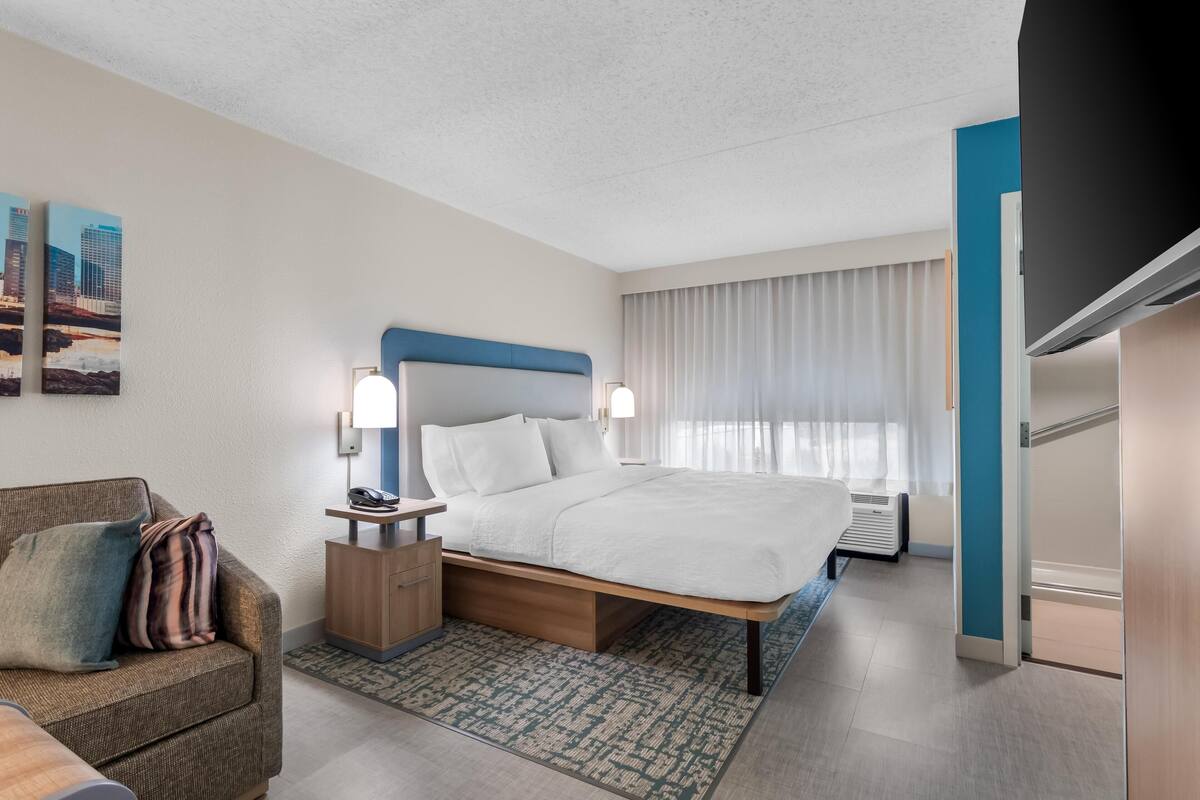 Et moderne hotelværelse med seng, sengebord, lampe og udsigt over byen fra vinduet.
